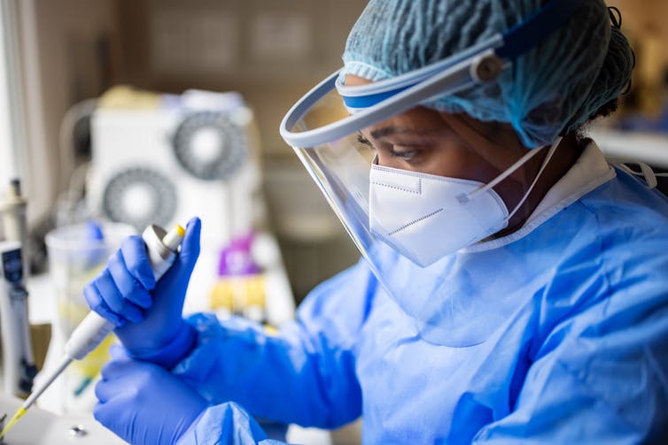 Researcher in PPE holding pipette in lab.