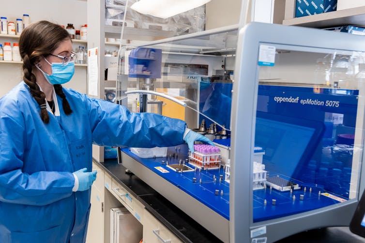 woman in PPE inserts specimens into lab equipment