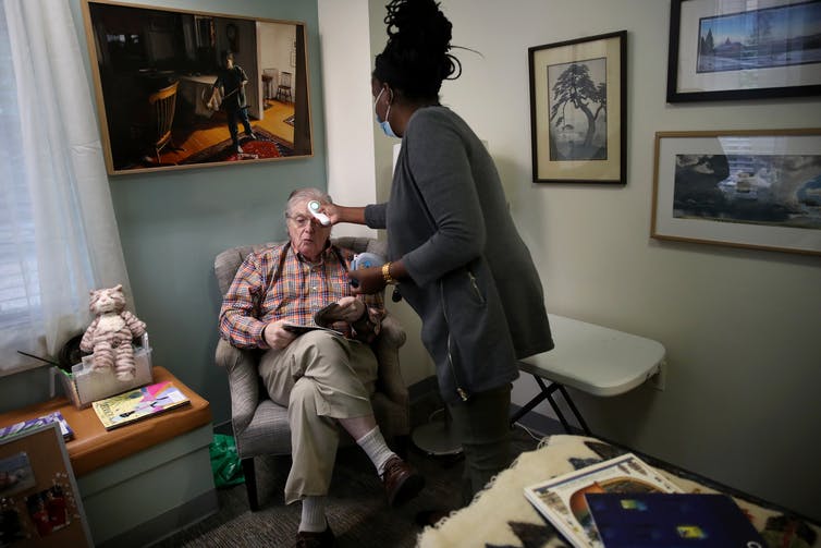 An assisted care facility staff member checks a resident's temperature