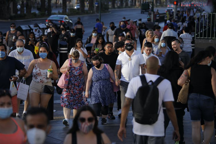 Crowds of people walking on sidewalks in Las Vegas, some wearing masks, some not.