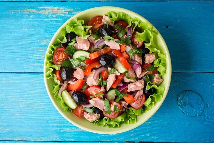 Salad with vegetables and tuna on rustic blue wooden table. Top view.