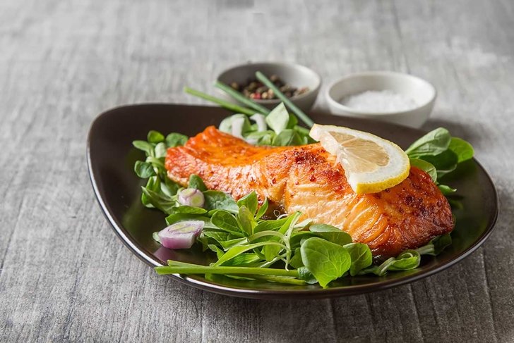 One piece of baked salmon grilled pepper lemon and salt on a brown plate with lettuce leaves. wood background