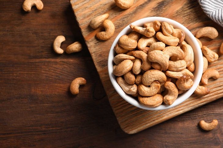 Tasty cashew nuts in bowl on wooden table, top view