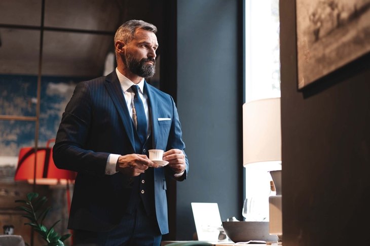 Enjoying fresh coffee while working. Confident man in smart casual wear holding coffee cup at his working place in office