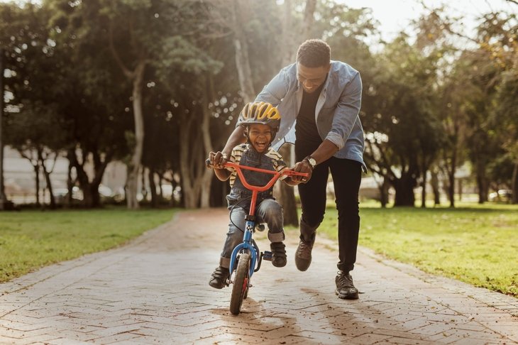 Boy learning to ride a bicycle with his father in park. Father teaching his son cycling at park.